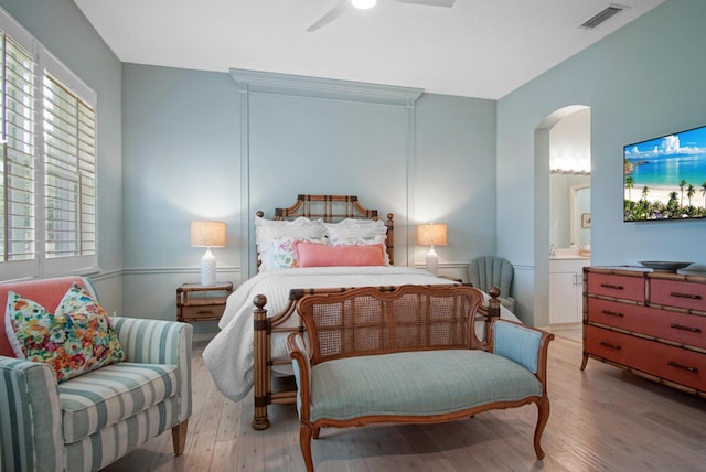 bedroom with arched walkways, wood finished floors, ensuite bath, and ceiling fan