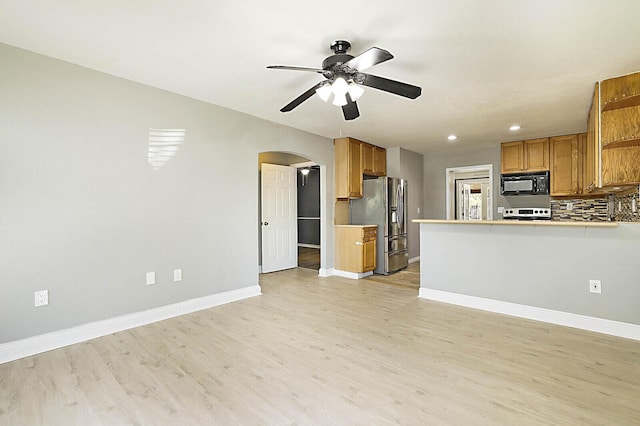 kitchen with appliances with stainless steel finishes, open shelves, arched walkways, ceiling fan, and light wood-style floors