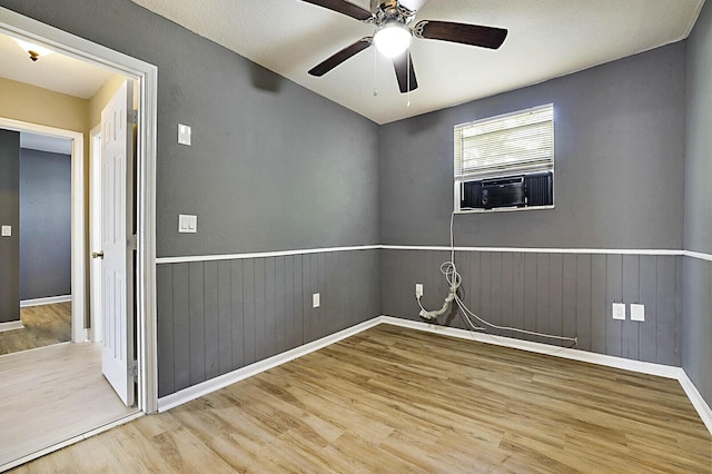 spare room with wood finished floors, cooling unit, ceiling fan, a wainscoted wall, and baseboards