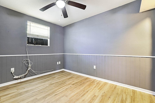 empty room with wood finished floors, a ceiling fan, cooling unit, and wainscoting