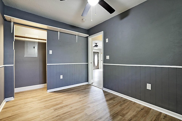 unfurnished bedroom with wood finished floors, a closet, a wainscoted wall, ceiling fan, and baseboards
