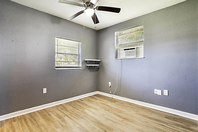 unfurnished room featuring wood finished floors, healthy amount of natural light, cooling unit, baseboards, and a textured wall