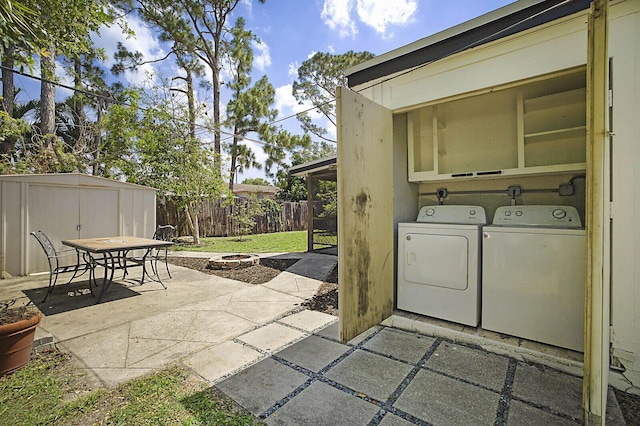view of patio featuring separate washer and dryer, a fire pit, a shed, a fenced backyard, and an outdoor structure