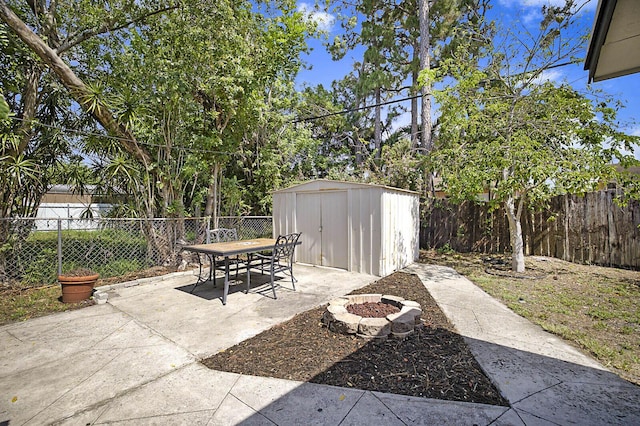 view of patio featuring a storage shed, outdoor dining space, a fire pit, an outbuilding, and a fenced backyard