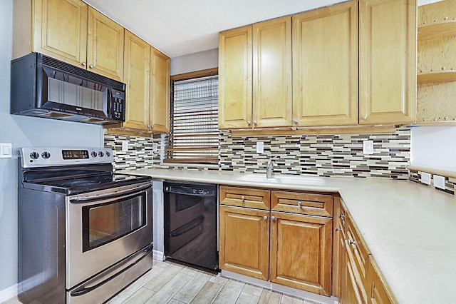 kitchen featuring black appliances, a sink, light countertops, decorative backsplash, and light wood finished floors