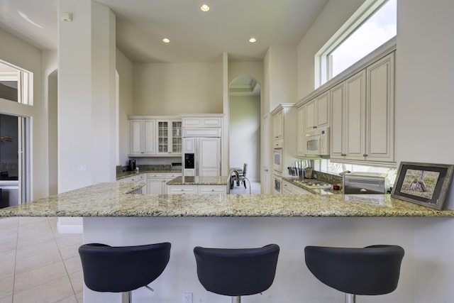 212 Montant Dr, Palm Beach Gardens, FL 33410 - kitchen with arched walkways, white microwave, paneled fridge, a peninsula, and light stone counters