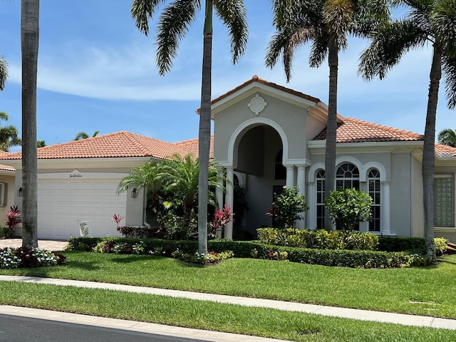 mediterranean / spanish home with a tiled roof, a garage, a front lawn, and stucco siding