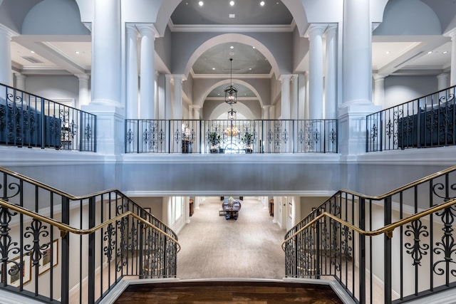 staircase featuring ornamental molding, decorative columns, a chandelier, wood finished floors, and a towering ceiling