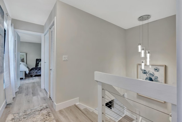 corridor featuring an upstairs landing, light wood-type flooring, and baseboards