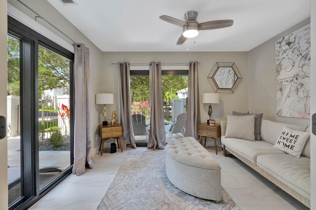 living room with healthy amount of natural light, ceiling fan, and marble finish flooring