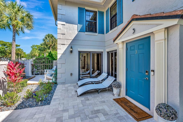 view of exterior entry featuring stucco siding, a patio, and fence