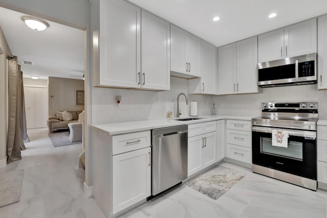 kitchen with stainless steel appliances, a sink, backsplash, light countertops, and light marble finish flooring
