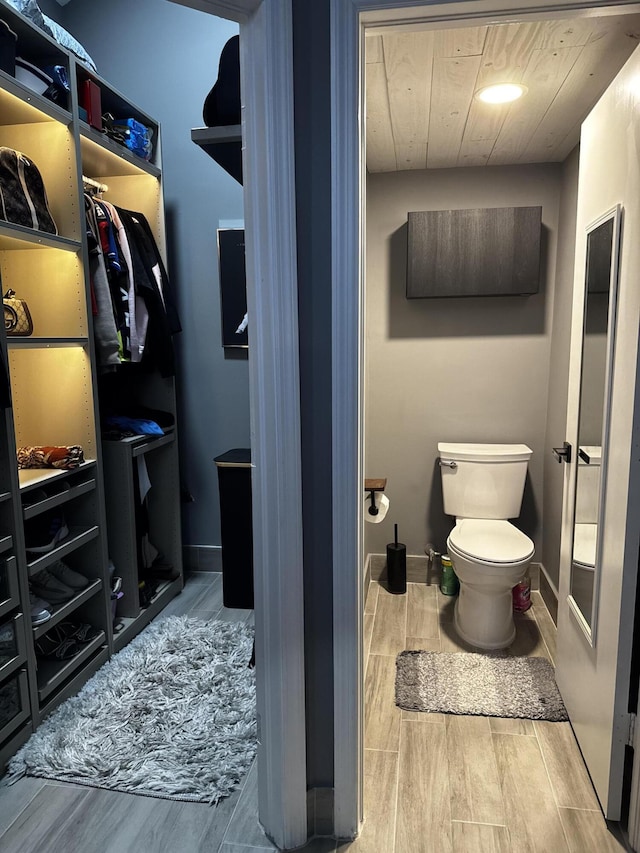 bathroom with wood tiled floors, toilet, baseboards, and a walk in closet