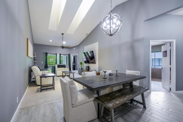 dining space featuring high vaulted ceiling, baseboards, light wood-style flooring, a skylight, and a chandelier