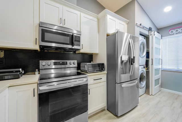kitchen featuring appliances with stainless steel finishes, stacked washer / drying machine, white cabinets, light countertops, and a barn door