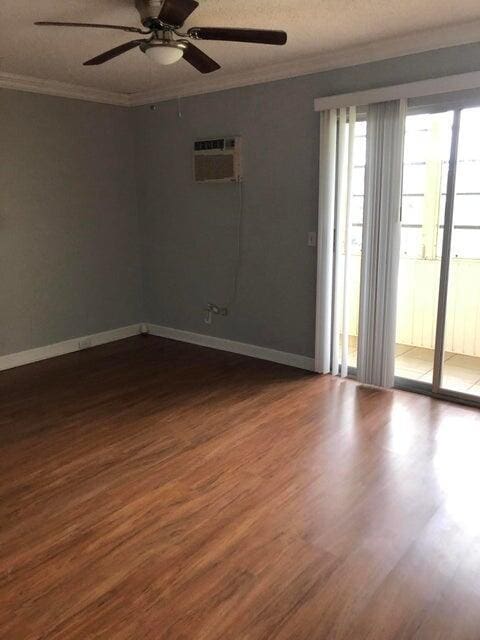 261 Suffolk Unit G, Boca Raton, FL 33434 - empty room with ornamental molding, a wall unit AC, dark wood-style flooring, ceiling fan, and baseboards