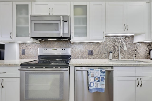 kitchen with appliances with stainless steel finishes, white cabinetry, a sink, decorative backsplash, and light stone counters
