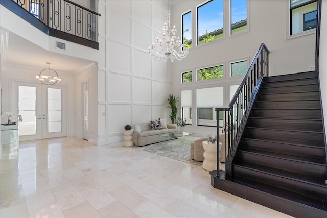 entrance foyer with a chandelier, a decorative wall, a towering ceiling, stairway, and french doors