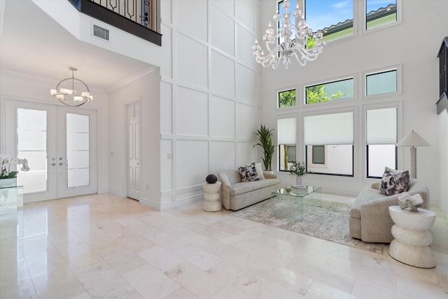 living room featuring a chandelier, a high ceiling, a decorative wall, french doors, and ornamental molding