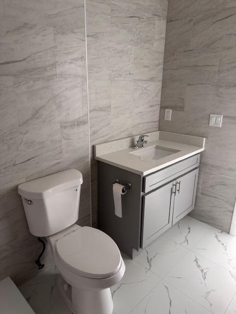 21 Walcott Dr, Boynton Beach, FL 33426 - bathroom with marble finish floors, tile walls, toilet, and vanity