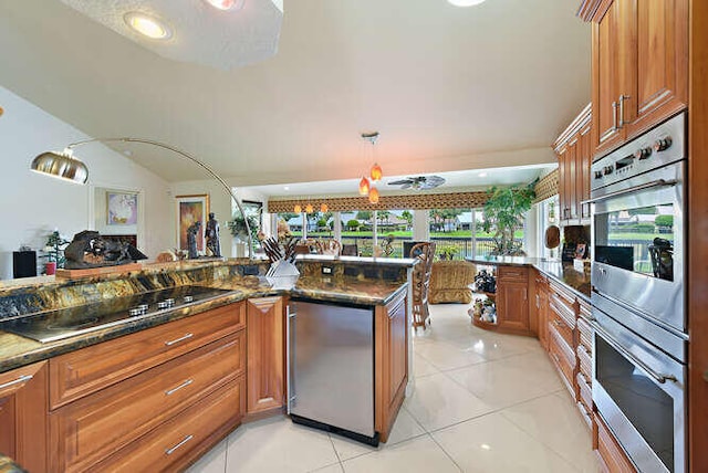 150 Beach Summit Ct, Jupiter, FL 33477 - kitchen featuring black electric cooktop, brown cabinetry, stainless steel double oven, light tile patterned flooring, and dark stone counters