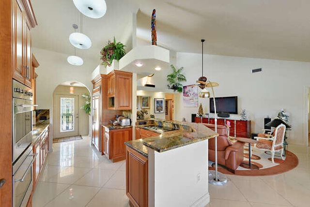 150 Beach Summit Ct, Jupiter, FL 33477 - kitchen with high vaulted ceiling, brown cabinets, dark stone counters, light tile patterned flooring, and arched walkways