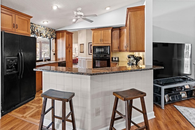 15180 69th Dr N, Palm Beach Gardens, FL 33418 - kitchen featuring black appliances, lofted ceiling, brown cabinetry, a peninsula, and a sink
