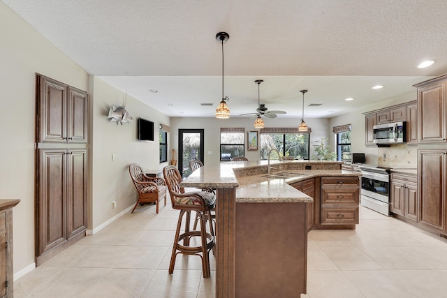 11195 N 159th Ct N, Jupiter, FL 33478 - kitchen with appliances with stainless steel finishes, a sink, a breakfast bar area, a ceiling fan, and light tile patterned floors