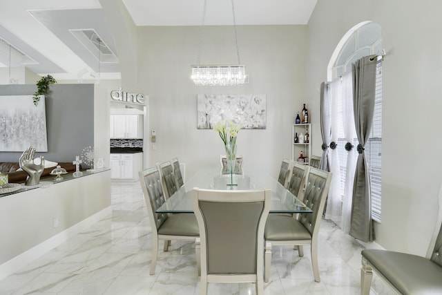 dining space with a chandelier, light marble finish floors, and baseboards