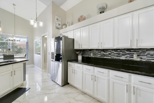 kitchen with stainless steel fridge with ice dispenser, a chandelier, tasteful backsplash, light marble finish flooring, and white cabinetry