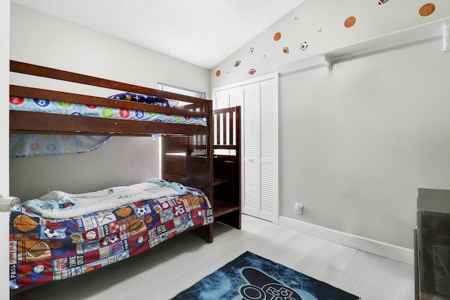 bedroom with a closet, lofted ceiling, baseboards, and wood finished floors