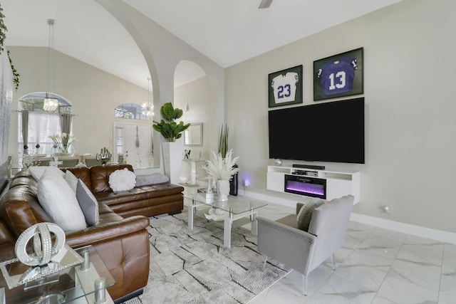 living area featuring lofted ceiling, arched walkways, marble finish floors, and baseboards