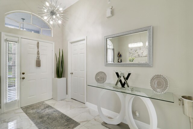 entrance foyer with light marble finish flooring, baseboards, and a chandelier