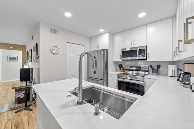 3561 Pine Tree Ct Unit A-2, Greenacres, FL 33463 - kitchen featuring appliances with stainless steel finishes, light stone counters, light wood-type flooring, white cabinets, and tasteful backsplash