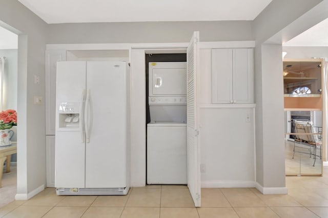 kitchen with white refrigerator with ice dispenser, stacked washer and clothes dryer, baseboards, and white cabinetry