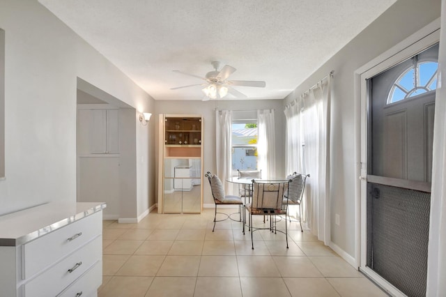dining space featuring a ceiling fan, light tile patterned floors, baseboards, and a textured ceiling