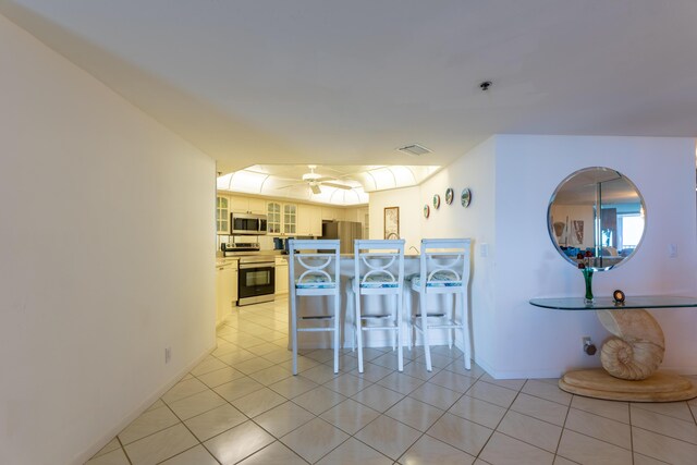 kitchen featuring appliances with stainless steel finishes, ceiling fan, glass insert cabinets, a kitchen breakfast bar, and a peninsula