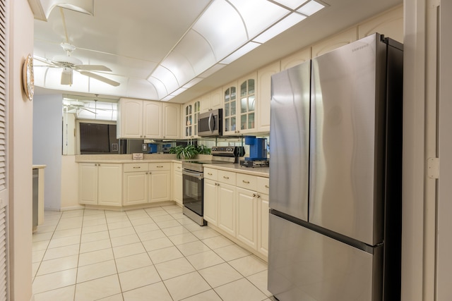 kitchen featuring appliances with stainless steel finishes, a ceiling fan, light tile patterned flooring, glass insert cabinets, and light countertops