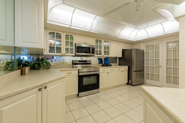 kitchen featuring appliances with stainless steel finishes, light tile patterned floors, light countertops, glass insert cabinets, and white cabinets