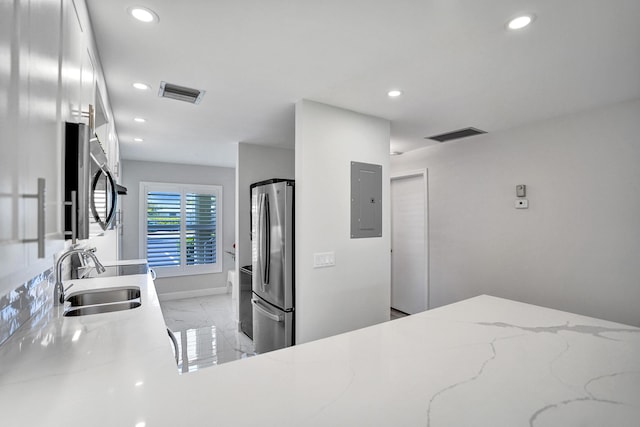kitchen featuring freestanding refrigerator, a sink, electric panel, recessed lighting, and light marble finish floors
