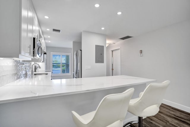 kitchen with stainless steel appliances, a peninsula, electric panel, dark wood finished floors, and white cabinetry
