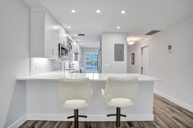 kitchen with stainless steel microwave, electric panel, light countertops, dark wood-style flooring, and a peninsula