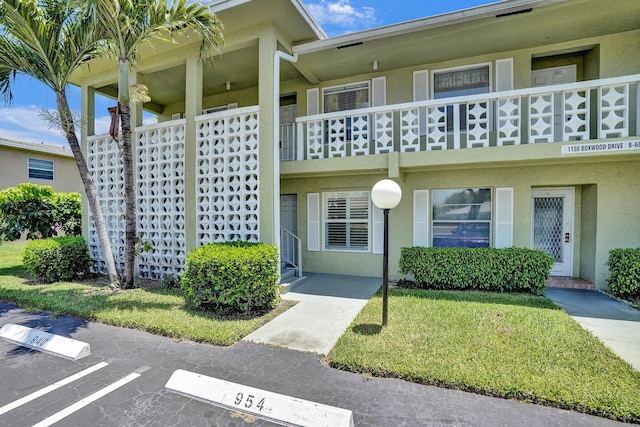entrance to property with uncovered parking, stucco siding, a yard, and a balcony