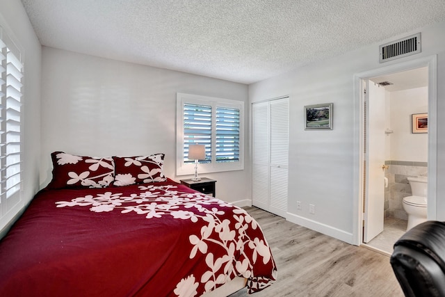 bedroom with wood finished floors, a textured ceiling, a closet, connected bathroom, and baseboards