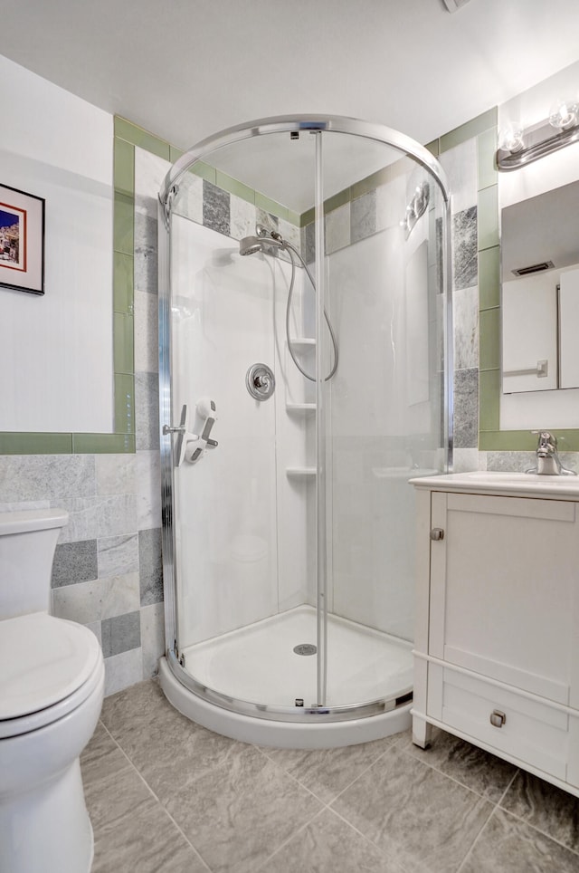bathroom featuring a shower stall, vanity, toilet, tile walls, and tile patterned floors
