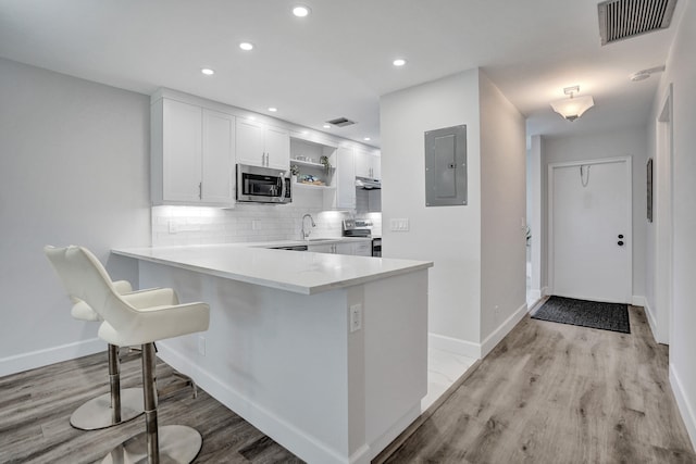 kitchen with electric panel, stainless steel appliances, open shelves, white cabinets, and backsplash