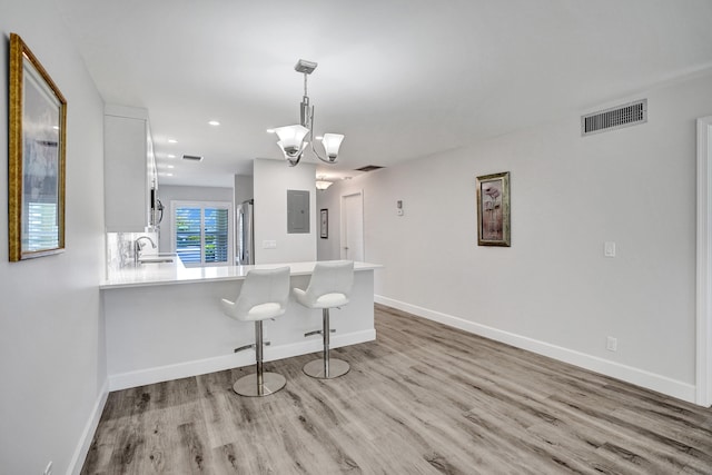 kitchen with stainless steel refrigerator, light wood-style flooring, light countertops, a chandelier, and a kitchen bar