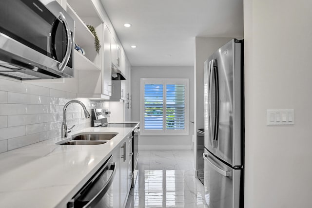 kitchen featuring stainless steel appliances, a sink, light marble finish flooring, baseboards, and tasteful backsplash