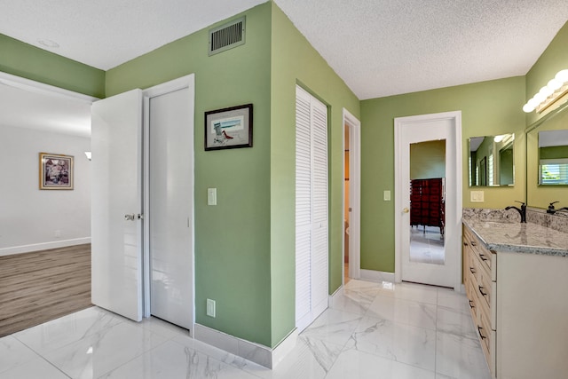 hall with baseboards, a sink, light marble finish flooring, and a textured ceiling