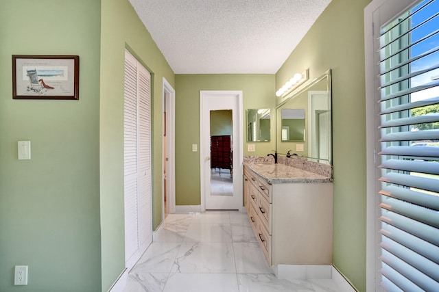 bathroom with marble look tiles, vanity, a textured ceiling, baseboards, and a closet